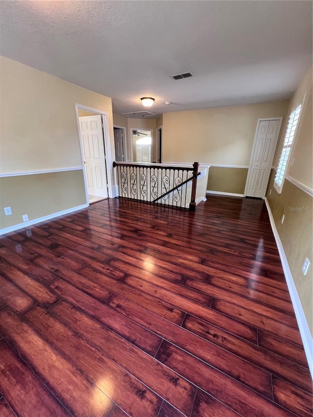 unfurnished room with dark wood-type flooring, visible vents, a textured ceiling, and baseboards