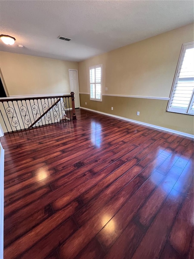 unfurnished room featuring baseboards, visible vents, dark wood finished floors, and a textured ceiling