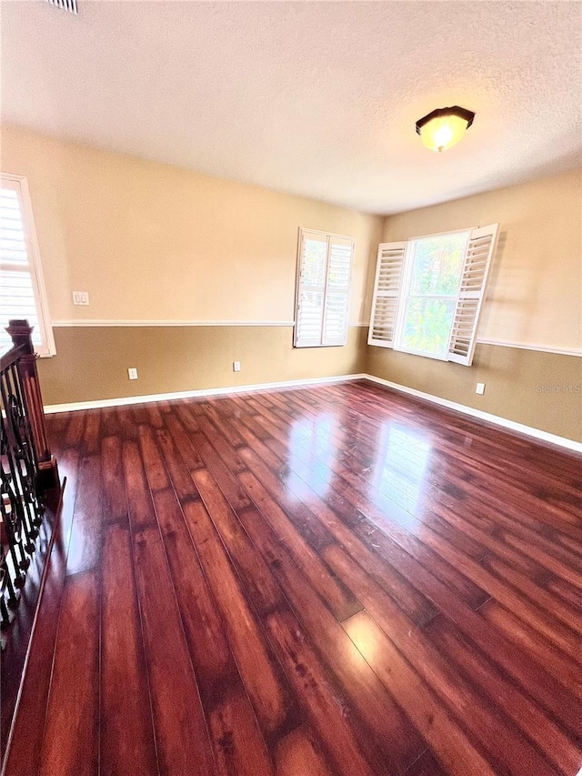 empty room with dark wood-style floors, a textured ceiling, and baseboards