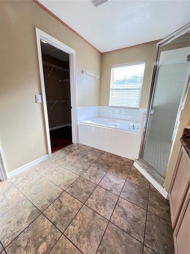 bathroom with a textured ceiling, ornamental molding, a bath, a stall shower, and a walk in closet