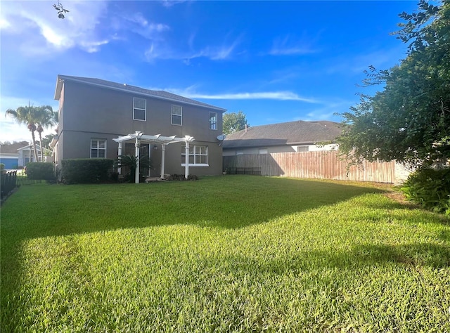 rear view of property with a yard, stucco siding, fence, and a pergola