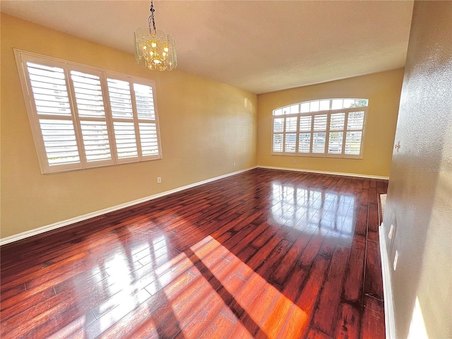 unfurnished room featuring a notable chandelier, baseboards, and wood finished floors