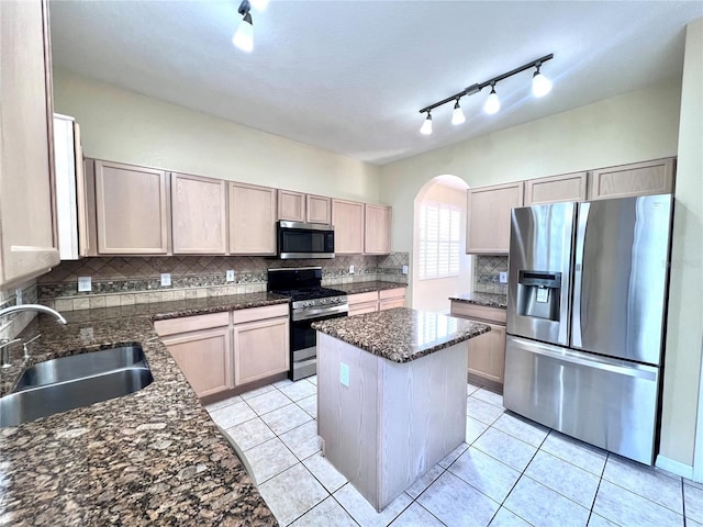 kitchen with dark stone counters, a kitchen island, stainless steel appliances, light brown cabinets, and a sink