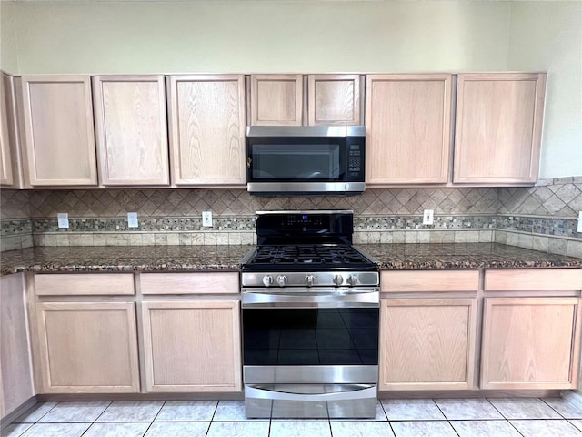 kitchen with appliances with stainless steel finishes, backsplash, dark stone countertops, and light brown cabinetry