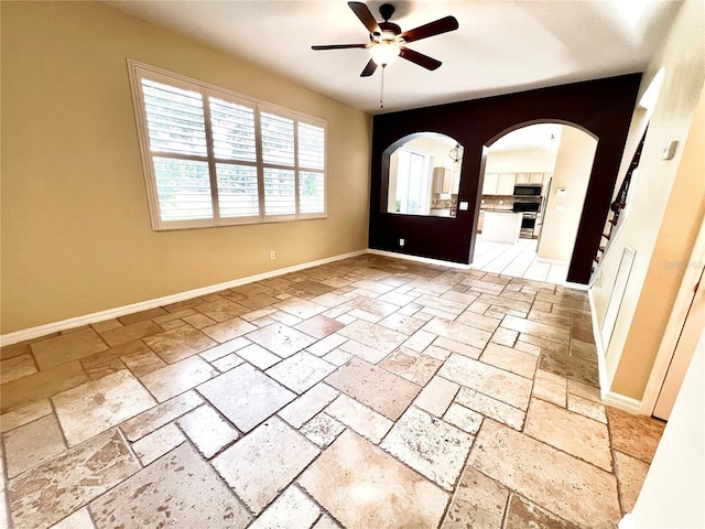 entrance foyer with arched walkways, stone tile floors, a ceiling fan, and baseboards