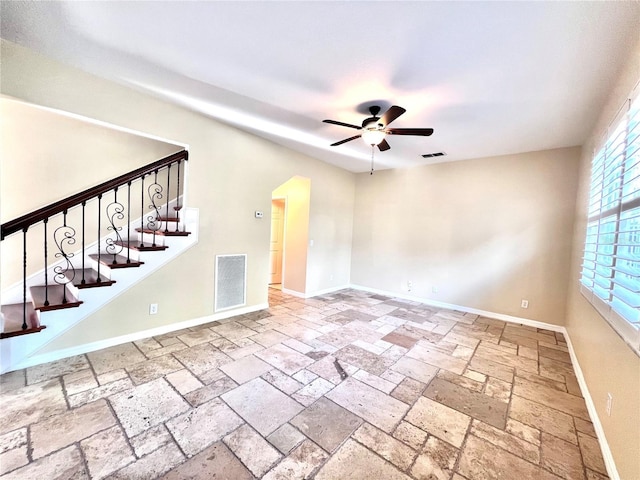 spare room featuring a ceiling fan, stone tile flooring, visible vents, and baseboards