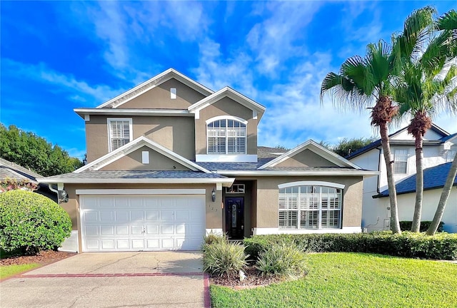 traditional-style house featuring a shingled roof, driveway, a front lawn, and stucco siding