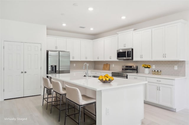 kitchen featuring a center island with sink, a kitchen breakfast bar, white cabinets, sink, and stainless steel appliances