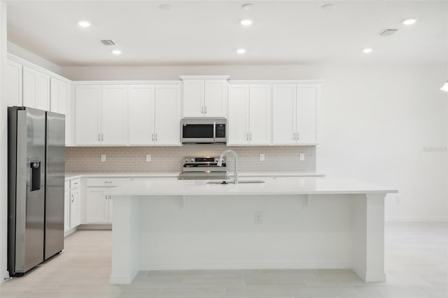 kitchen featuring white cabinets, sink, stainless steel appliances, and an island with sink