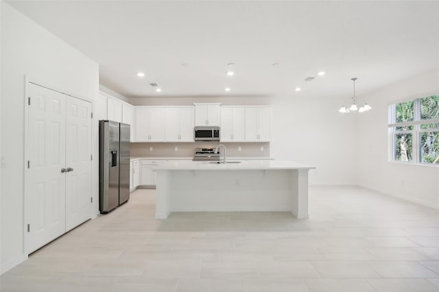 kitchen with pendant lighting, a kitchen island with sink, white cabinets, appliances with stainless steel finishes, and tasteful backsplash