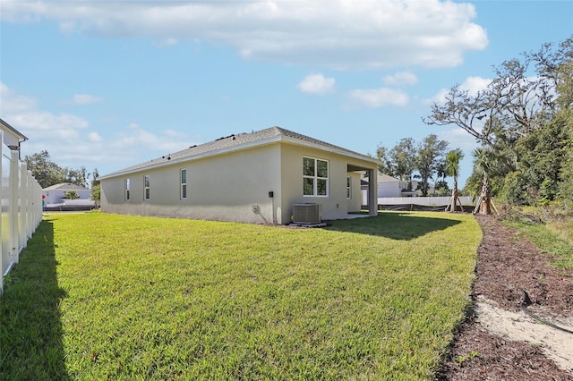 rear view of property featuring central air condition unit and a lawn