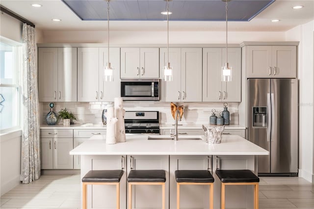 kitchen featuring a kitchen island with sink, appliances with stainless steel finishes, pendant lighting, and light countertops