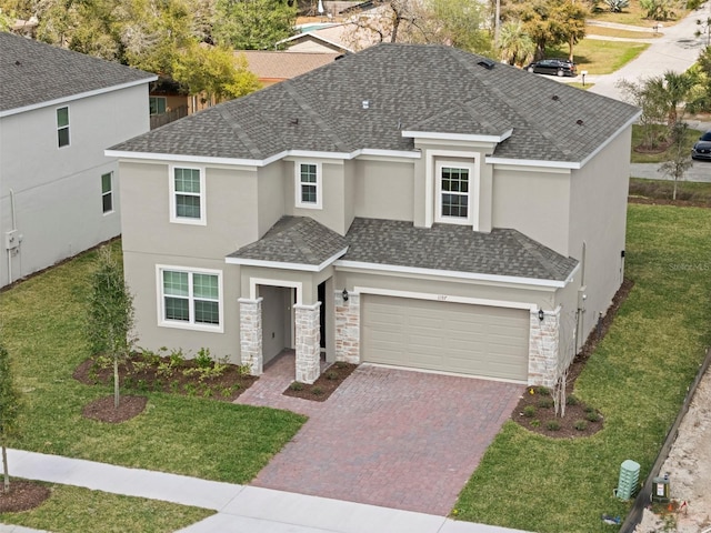 view of front of house featuring decorative driveway, a shingled roof, a garage, stone siding, and a front lawn