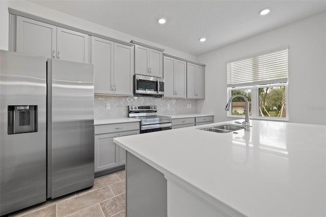 kitchen featuring a sink, light countertops, appliances with stainless steel finishes, gray cabinets, and backsplash