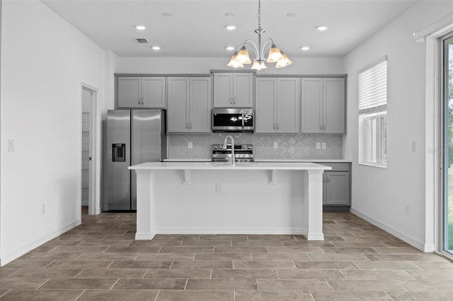 kitchen featuring stainless steel appliances, gray cabinets, and a kitchen island with sink