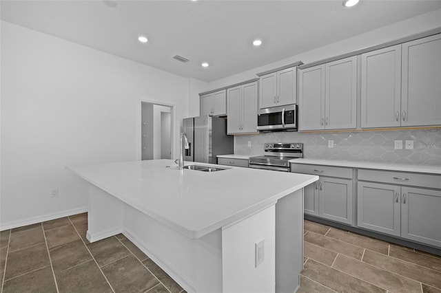 kitchen with stainless steel appliances, visible vents, gray cabinets, tasteful backsplash, and a center island with sink