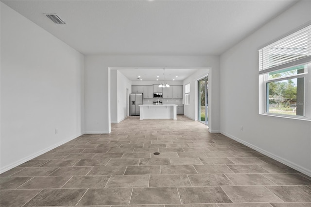 unfurnished living room with an inviting chandelier, baseboards, visible vents, and a wealth of natural light