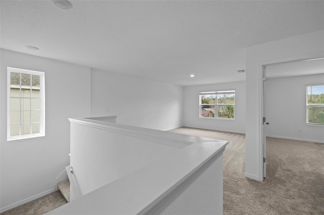 hallway featuring light carpet, plenty of natural light, visible vents, and baseboards