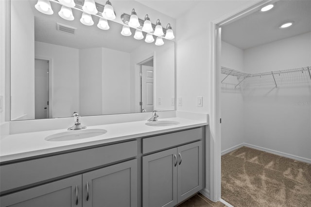 bathroom with a walk in closet, visible vents, a sink, and double vanity