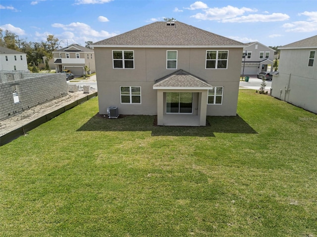 rear view of property featuring stucco siding, roof with shingles, a lawn, and central AC unit