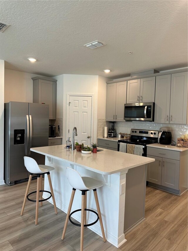 kitchen with a kitchen bar, light hardwood / wood-style flooring, stainless steel appliances, and tasteful backsplash