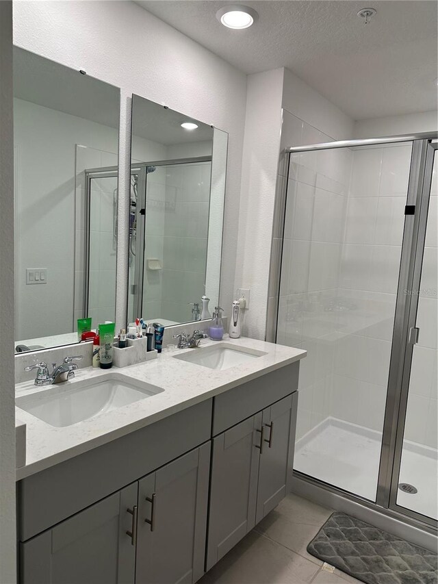 bathroom with tile patterned floors, a shower with door, and dual bowl vanity