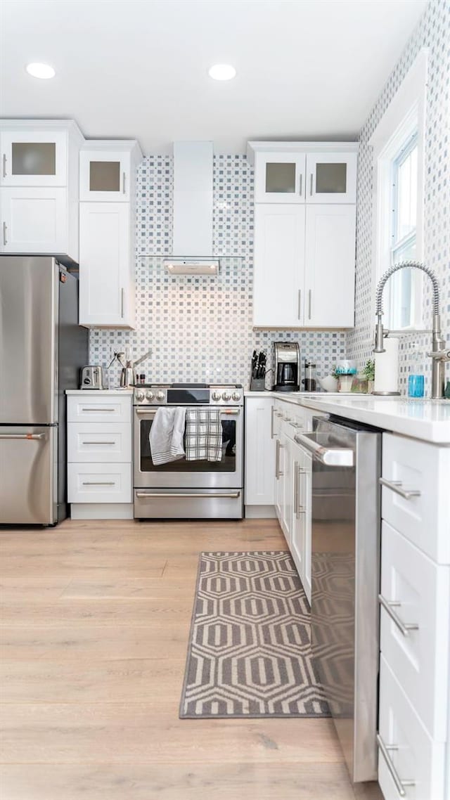 kitchen with appliances with stainless steel finishes, white cabinets, and wall chimney exhaust hood