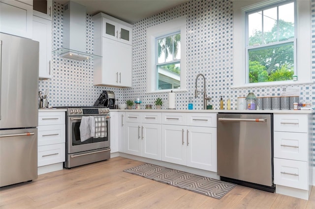 kitchen featuring stainless steel appliances, white cabinets, light hardwood / wood-style floors, and wall chimney exhaust hood