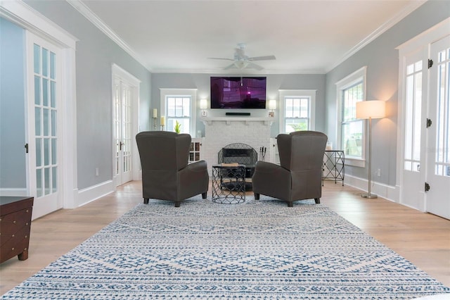 living room featuring crown molding, ceiling fan, a fireplace, and light hardwood / wood-style flooring