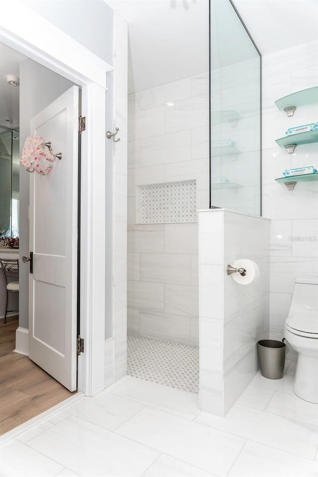 bathroom featuring a tile shower, tile patterned flooring, toilet, and tile walls