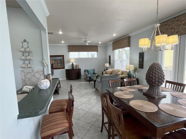 tiled dining room featuring ceiling fan with notable chandelier, ornamental molding, and a textured ceiling