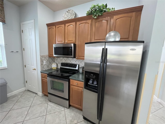 kitchen featuring light tile patterned floors, stainless steel appliances, tasteful backsplash, and brown cabinetry