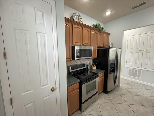 kitchen featuring light tile patterned flooring, decorative backsplash, appliances with stainless steel finishes, and a textured ceiling