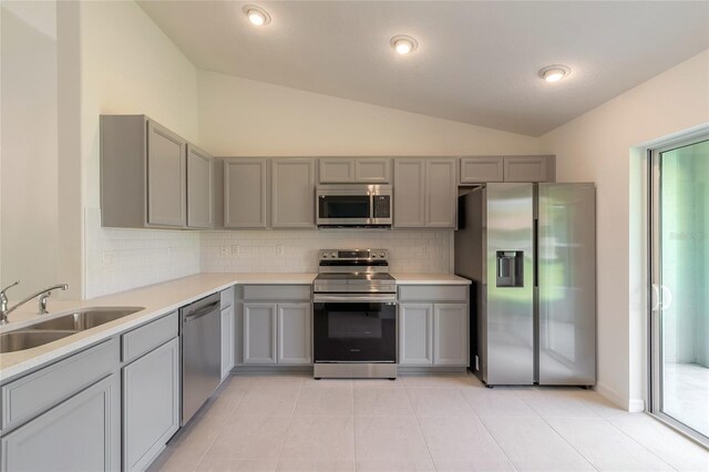 kitchen with stainless steel appliances, gray cabinetry, vaulted ceiling, backsplash, and light tile patterned floors