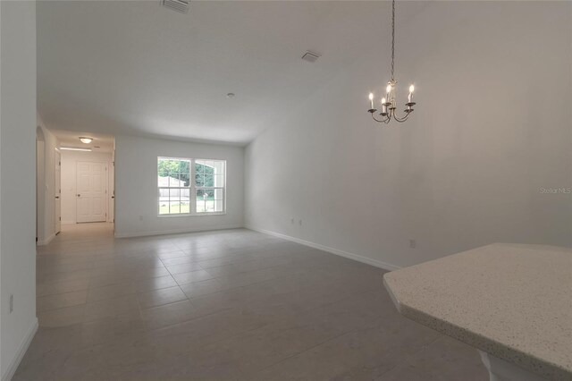 tiled spare room featuring a notable chandelier and vaulted ceiling