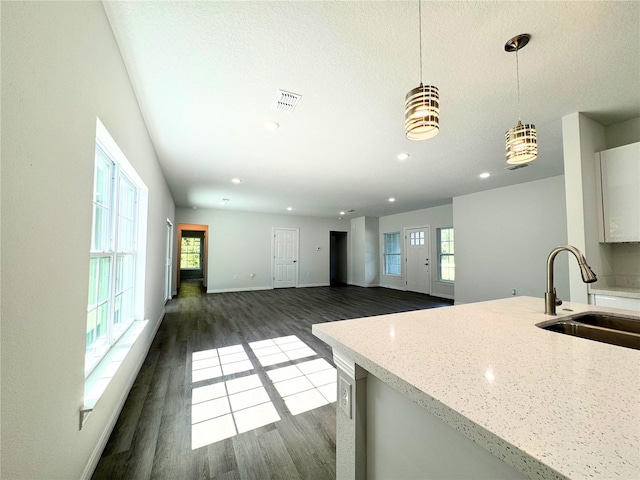 kitchen with sink, light stone counters, pendant lighting, and dark hardwood / wood-style floors