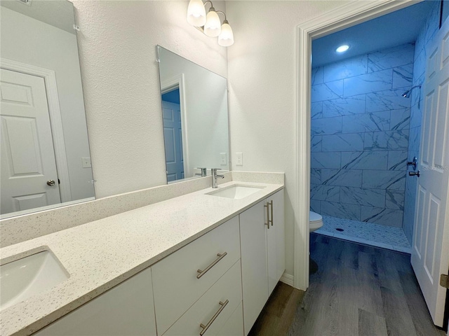 bathroom featuring wood-type flooring, double sink vanity, toilet, and a tile shower