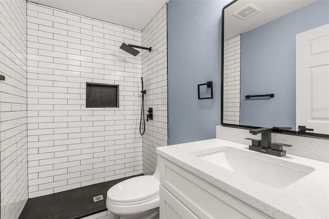 bathroom with vanity, tiled shower, and toilet