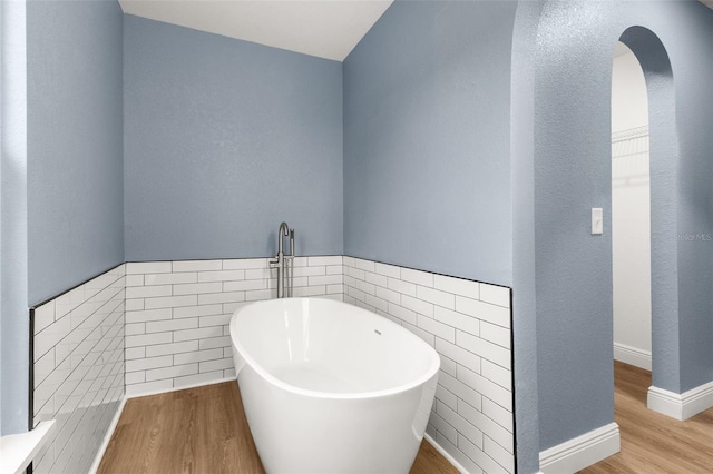 bathroom featuring hardwood / wood-style flooring, a tub, and tile walls