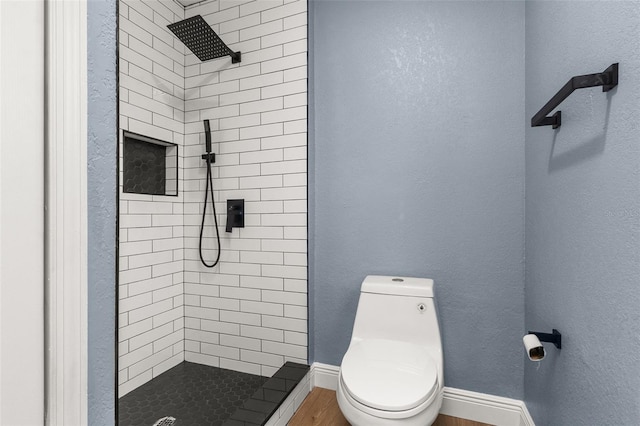 bathroom featuring hardwood / wood-style flooring, tiled shower, and toilet