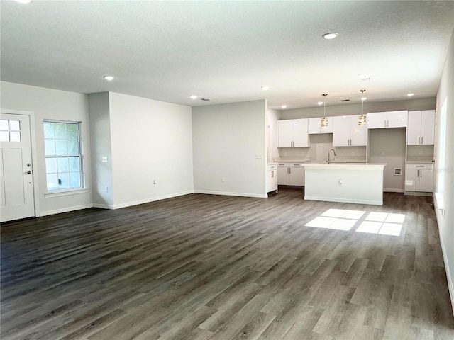 unfurnished living room featuring dark wood-type flooring, sink, and a textured ceiling