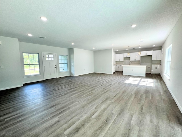 unfurnished living room with sink, a textured ceiling, and light wood-type flooring