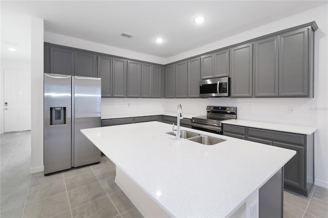 kitchen featuring gray cabinetry, stainless steel appliances, a center island with sink, and light tile patterned floors