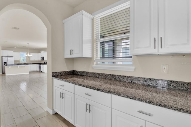 kitchen featuring stainless steel refrigerator with ice dispenser, pendant lighting, white cabinets, light tile patterned floors, and dark stone counters