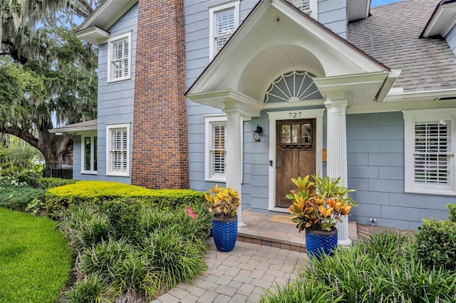 entrance to property featuring a shingled roof and a chimney