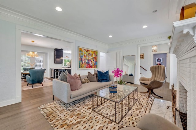 living room featuring crown molding, a fireplace, an inviting chandelier, wood finished floors, and baseboards