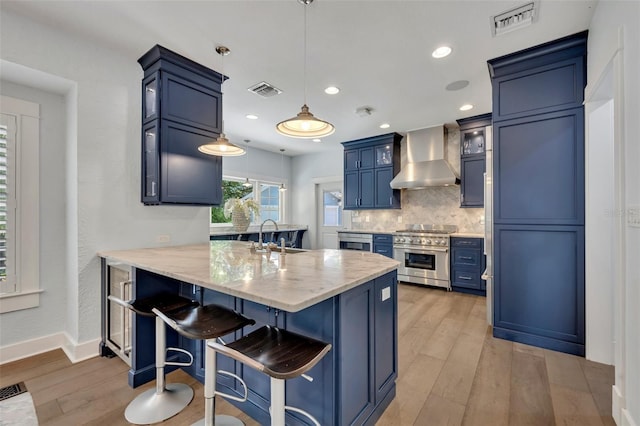 kitchen with blue cabinetry, hanging light fixtures, high end stainless steel range oven, glass insert cabinets, and wall chimney range hood