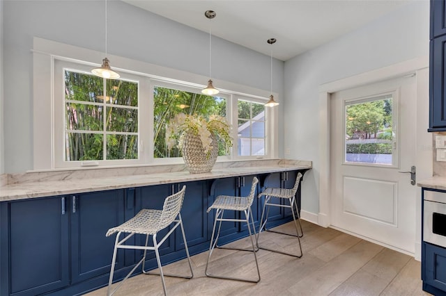 kitchen with blue cabinetry, light wood-type flooring, light stone counters, and pendant lighting