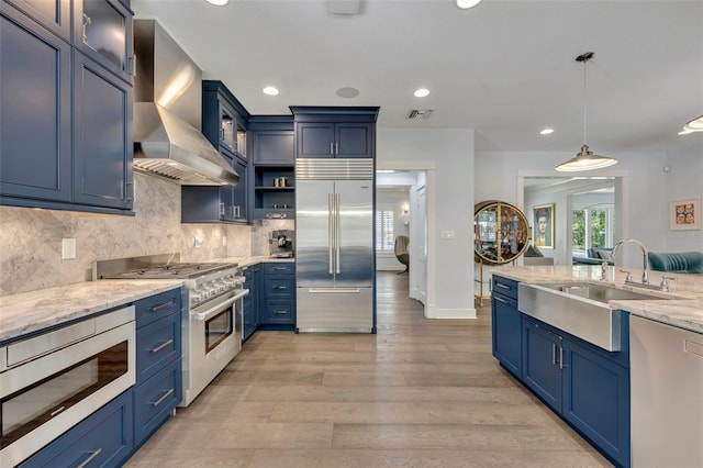 kitchen featuring glass insert cabinets, a sink, built in appliances, blue cabinets, and wall chimney exhaust hood