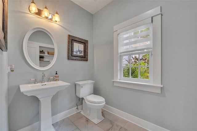 half bathroom featuring toilet, marble finish floor, baseboards, and a sink